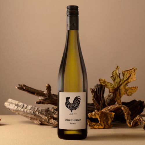 Eine Weißweinflasche mit einem schwarzen Hahn-Logo auf dem Etikett steht aufrecht auf einer beigen Fläche. Im Hintergrund sind getrocknete Blätter und Treibholz angeordnet, die eine herbstliche Atmosphäre schaffen.