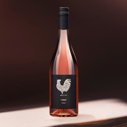 Eine Flasche Roséwein mit einem schwarzen Etikett, auf dem ein weißer Hahn und der Text "Malbec Rosé" abgebildet sind. Die Flasche steht auf einer sanft beleuchteten Fläche mit dunkelbraunem Hintergrund.