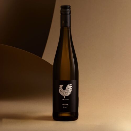 Eine Weinflasche mit einem schwarzen Etikett, auf dem ein weißer Hahn und der Text "PEZSGŐ" abgebildet sind, steht aufrecht auf einer beigen Fläche mit einem abstrakten Hintergrund in Braun und Gold.