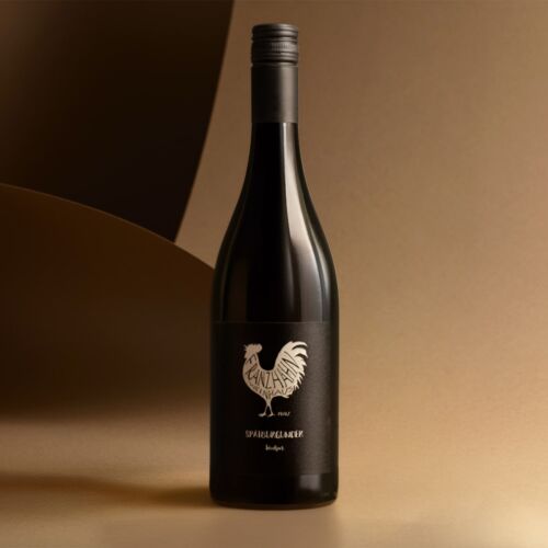 Eine Rotweinflasche mit einem schwarzen Etikett, auf dem ein weißer Hahn und der Schriftzug "Spätburgunder Pinot Noir" aufrecht vor einem glatten Hintergrund mit goldenem und braunem Farbverlauf stehen.
